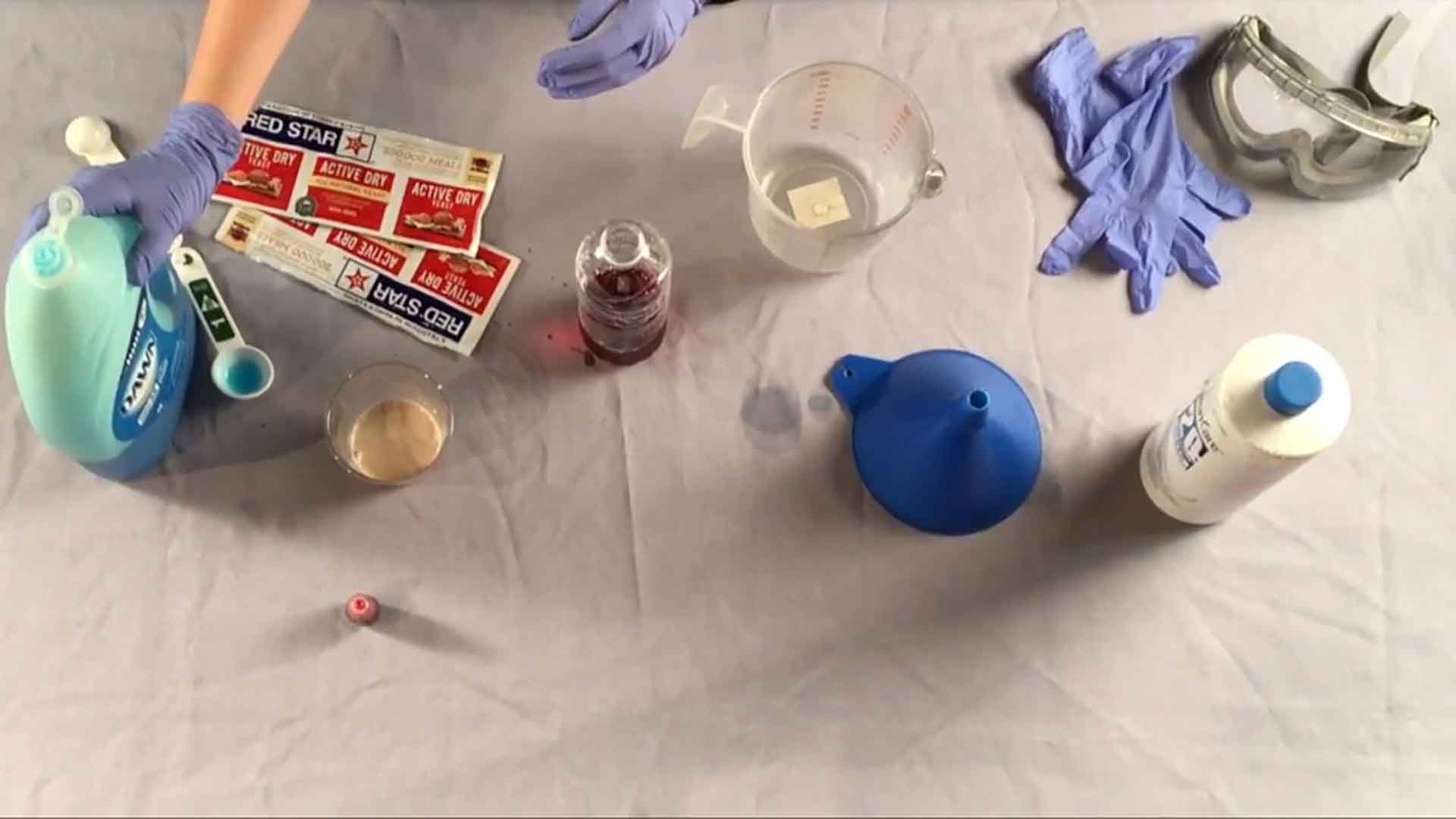 Different items on a table, including Dawn dish soup, a funnel, measuring cup, gloves, and safety goggles