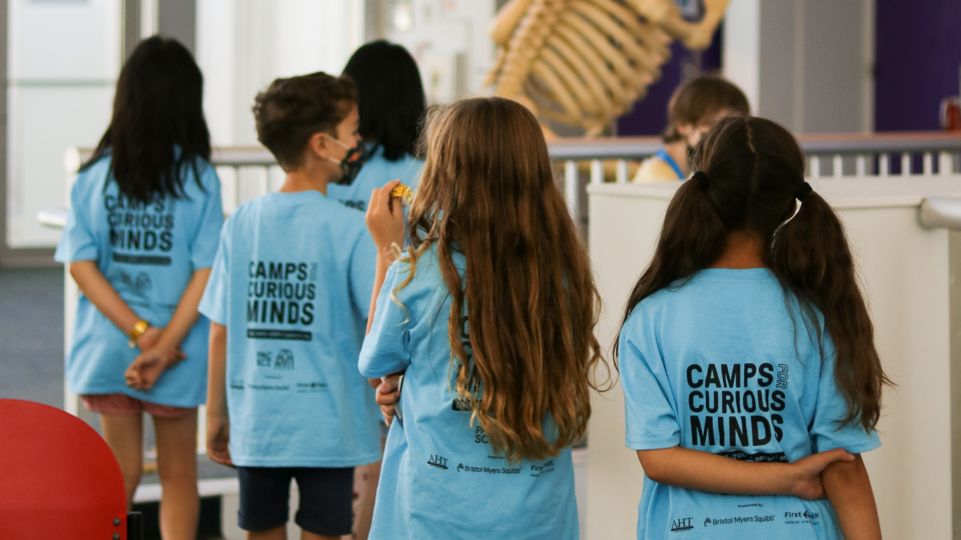 Four kids are standing in line with camps for curious minds shirts