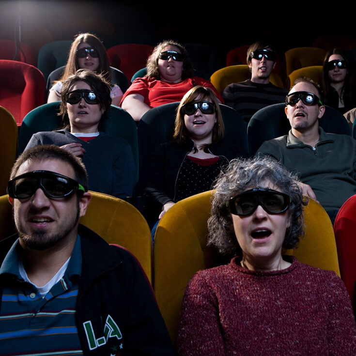 Movie goers wearing 3D glasses in colorful theater seats