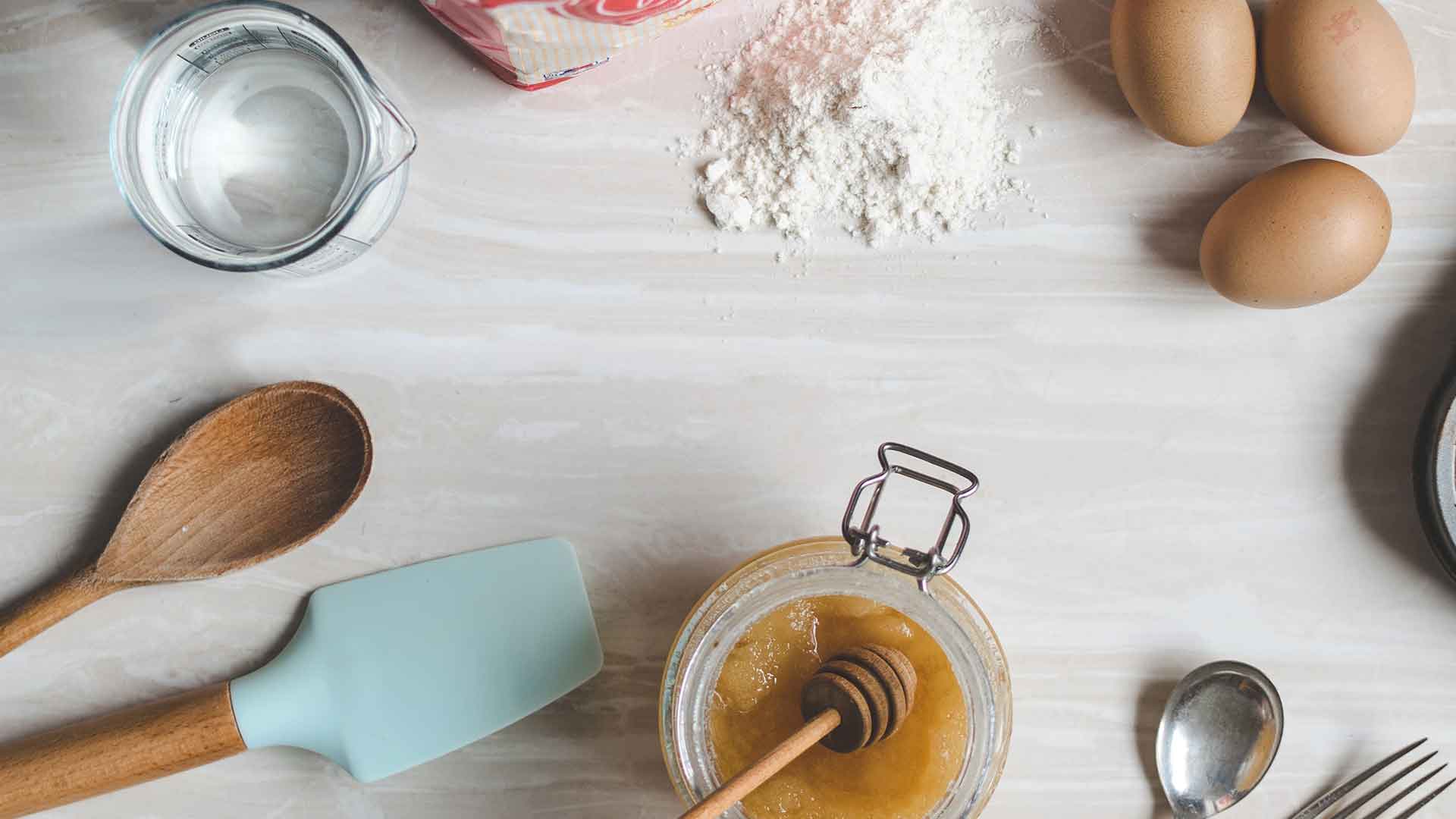 Baking ingredients like eggs and flour, and tools like a wooden spoon and spatula