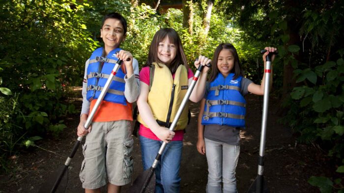 Three kids wearing vest and holding paddles