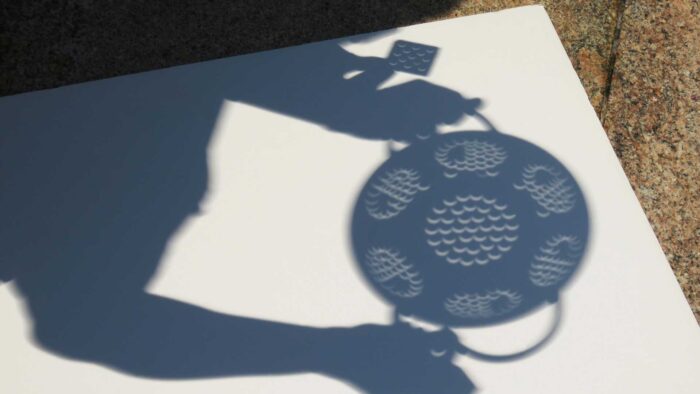 Someone holding a colander above a white piece of paper to show shadows during eclipse