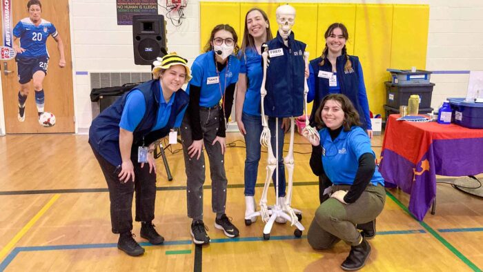 Five Science on Wheels educators with a plastic skeleton in a school gym