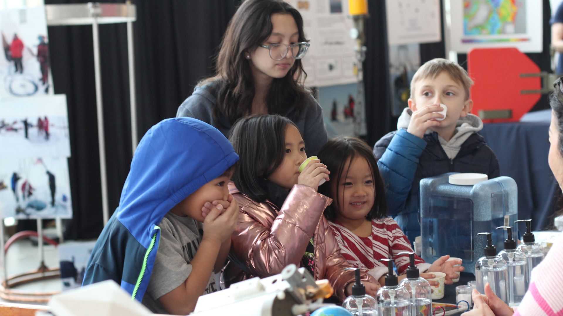 Four young children and an adult enthusiastically participate in a hands-on STEM activity during Polar Science Weekend 2024 at Pacific Science Center.