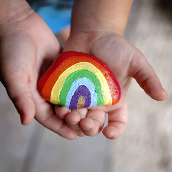 Child holding a rock painted like a rainbow
