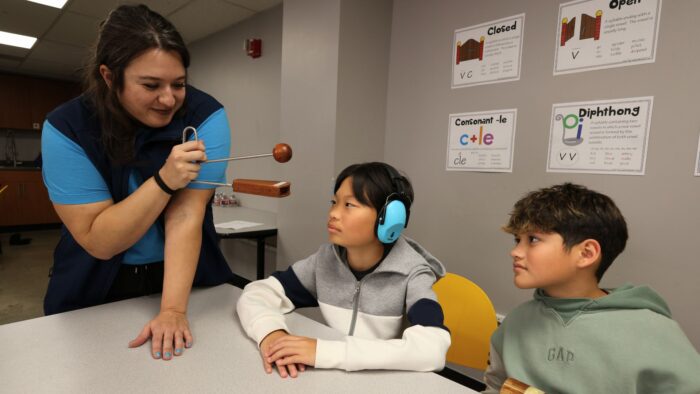Science on wheels educator is holding up a musical instrument in front of two students