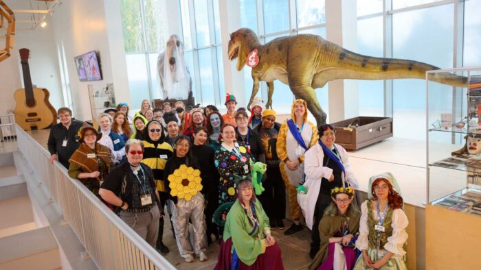 PacSci staff in costume posing in front of dinosaur statues