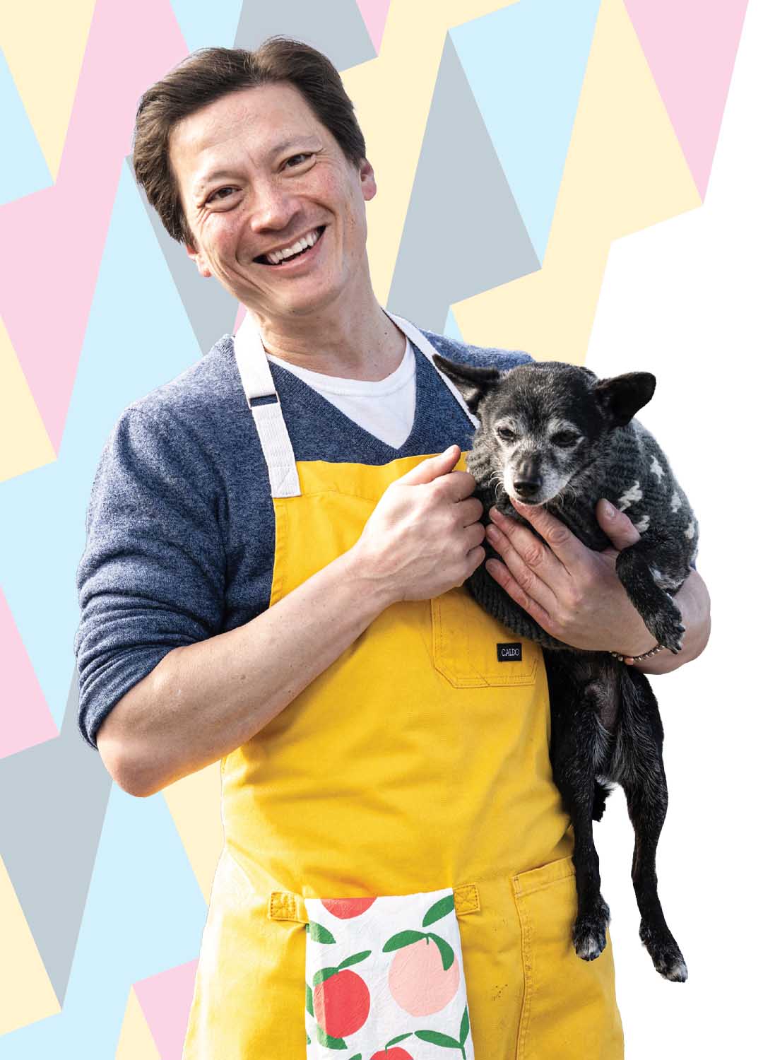 J. Kenji López-Alt wearing a yellow apron and holding a small dog